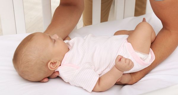 Schlafendes Baby wird auf den Rücken in seinem Bettchen gelegt.