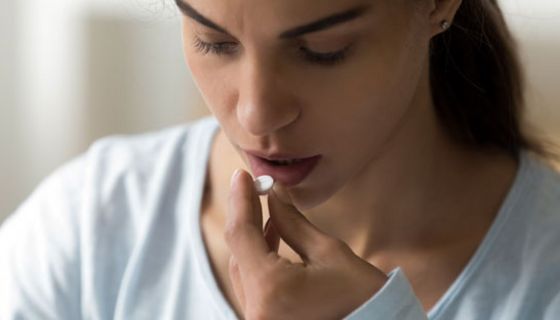 Junge Frau hält eine Tablette zwischen den Fingern und schaut skeptisch.