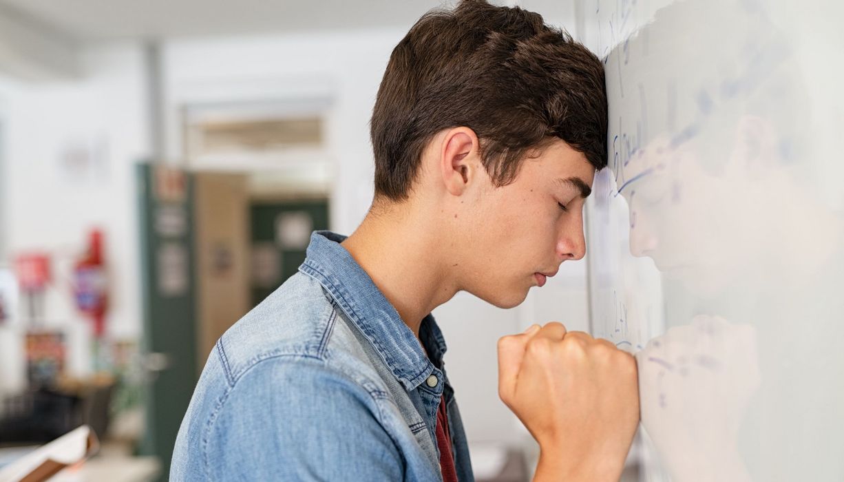 Jugendlicher, lehnt sich verzweifelt gegen ein Whiteboard.