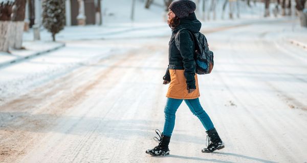 Frau in warmer Winterkleidung geht über eine vereiste Straße.