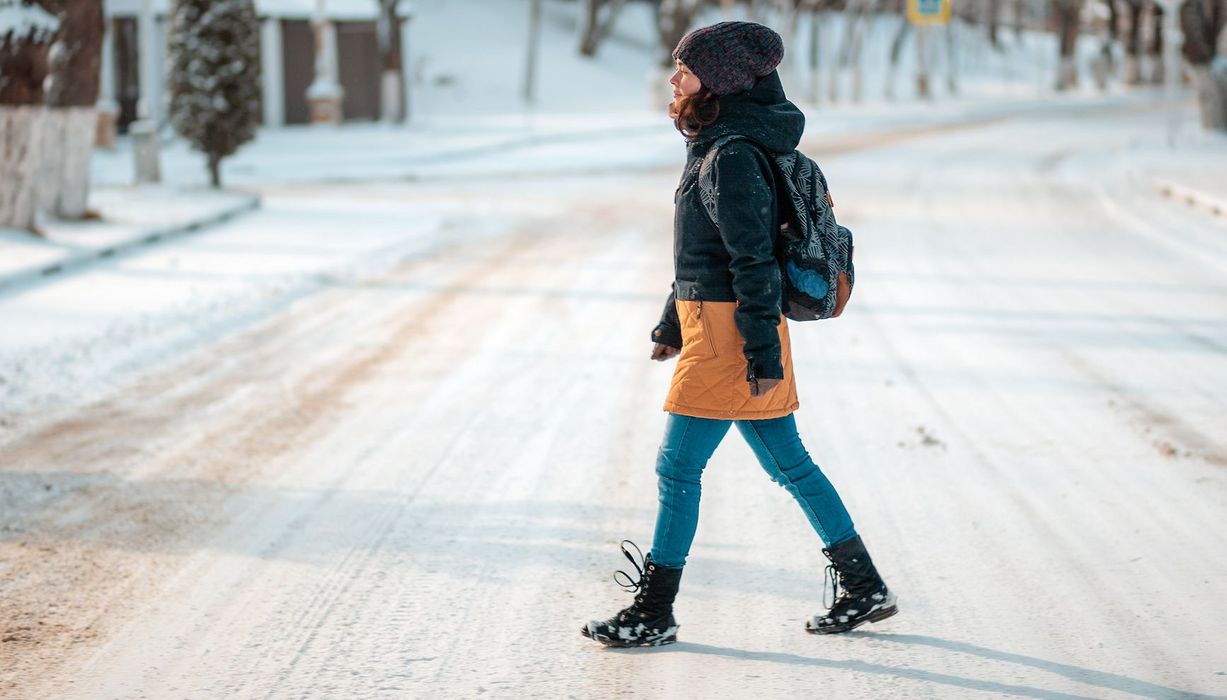 Frau in warmer Winterkleidung geht über eine vereiste Straße.