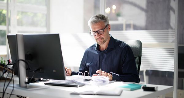 Mann sitzt im Büro am Schreibtisch und geht Dokumente durch