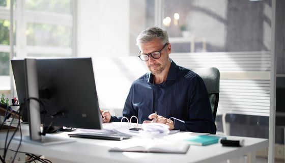 Mann sitzt im Büro am Schreibtisch und geht Dokumente durch