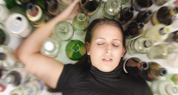 Junge betrunkene Frau liegt mit geschlossenen Augen inmitten leerer Alkoholflaschen
