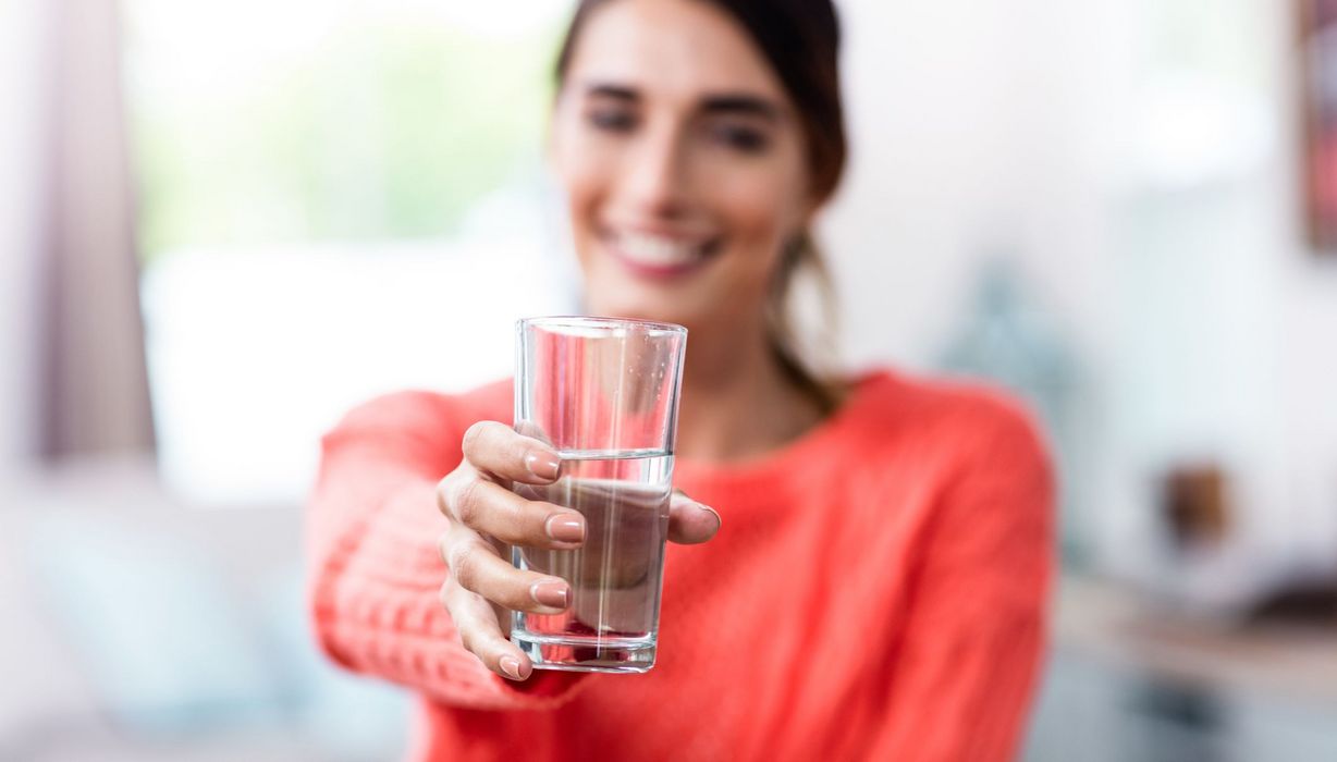 Junge Frau, hält ein Glas Wasser in die Kamera.