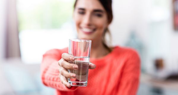 Junge Frau, hält ein Glas Wasser in die Kamera.