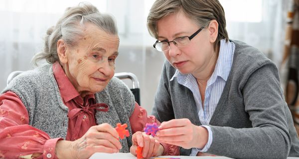 Ältere Frau löst ein Puzzle mit Pflegerin.