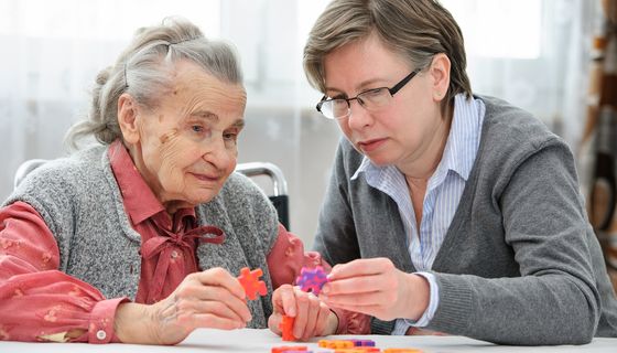 Ältere Frau löst ein Puzzle mit Pflegerin.