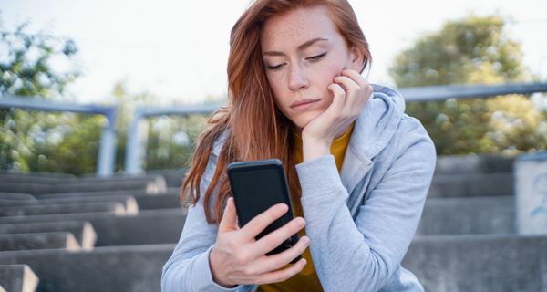 Junge Frau, schaut nachdenklich auf das Handy.