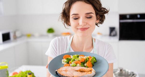 Frau zeigt einen Teller mit Lachs und Gemüse.
