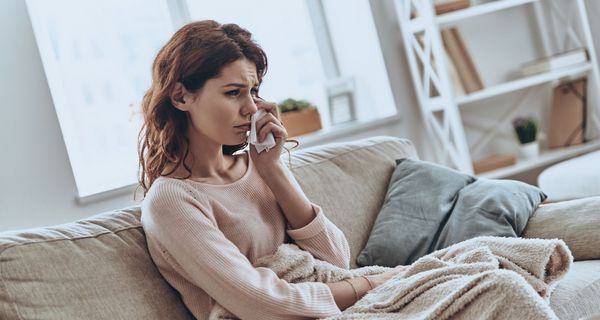 Eine junge Frau sitzt auf dem Sofa und weint.