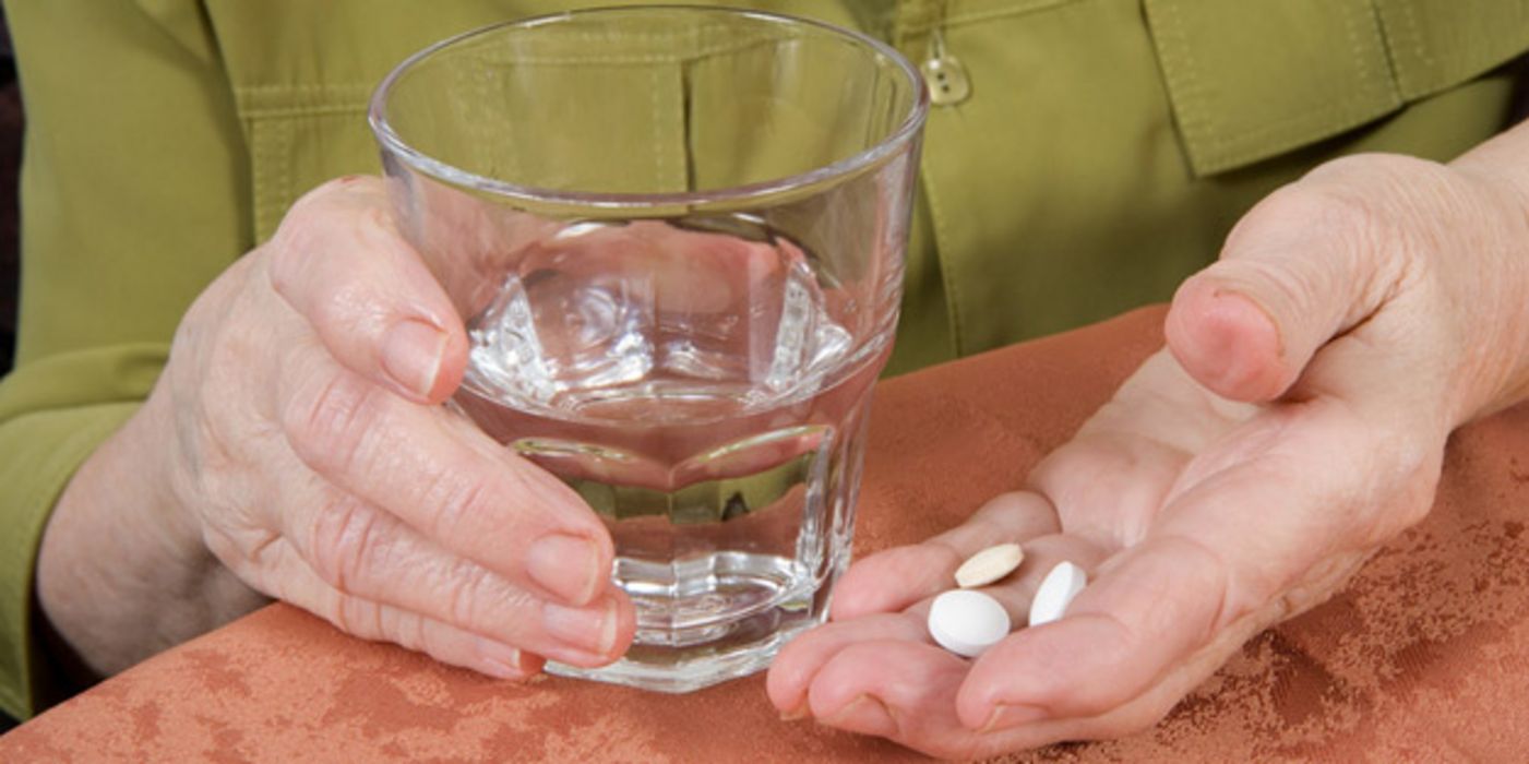 Ältere Frau mit Tabletten in der einen, einem Glas Wasser in der anderen Hand