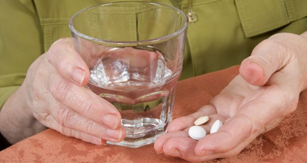 Ältere Frau mit Tabletten in der einen, einem Glas Wasser in der anderen Hand