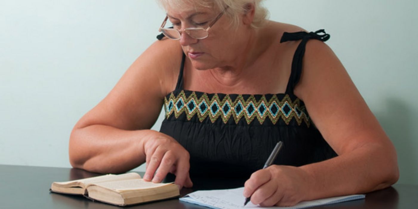 Frau um die 60 mit Brille schreibt etwas aus einem Buch ab