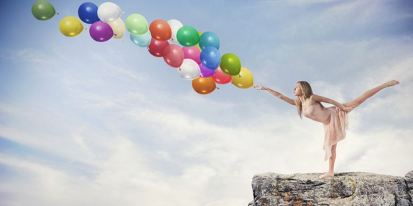 Tänzerin in der Waage stehend auf einem Felsvorsprung stößt mit ausgestrecktem Zeigefinger eine Traube Luftballons über dem Abgrund an
