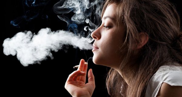 Profilansicht junger Frau in weißer Sommerbluse, Zigarette in der Hand, eine große Rauchwolke ausstoßend