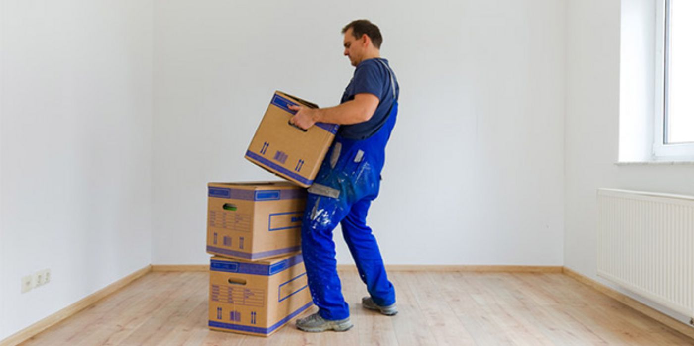 Umzugsprofi in blauer Arbeitslatzhose beim Heben eines Umzugskartons
