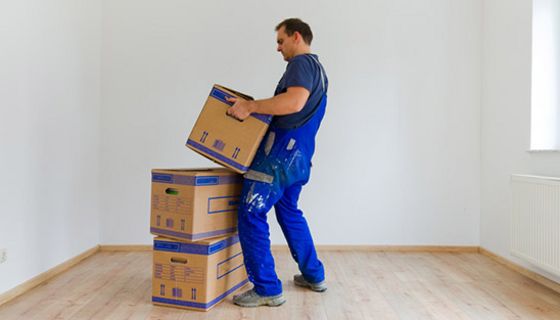 Umzugsprofi in blauer Arbeitslatzhose beim Heben eines Umzugskartons