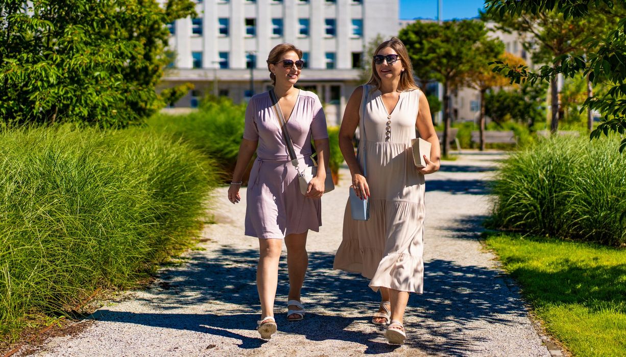 Zwei Frauen gehen im Stadtpark nebeneinander spazieren.