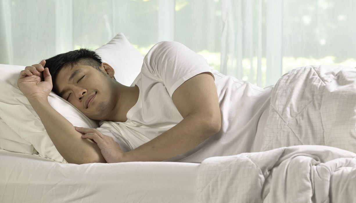 Ein junger Mann liegt morgens im Bett und schläft.