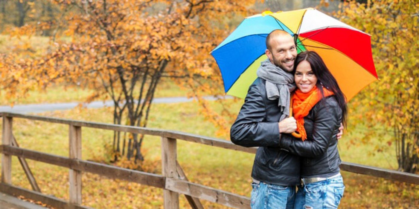 Junges Paar mit Regenschirm in Herbstlandschaft.