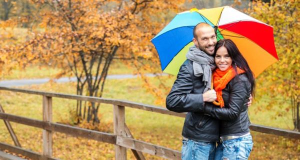 Junges Paar mit Regenschirm in Herbstlandschaft.