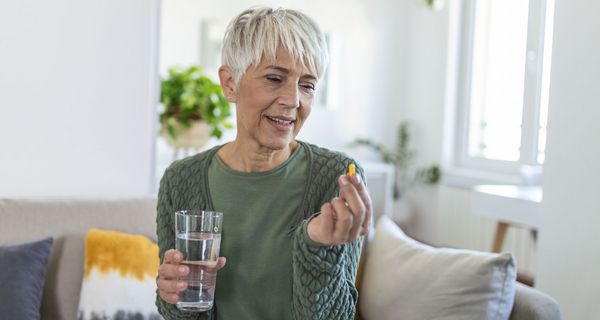 Seniorin, in einer Hand eine Tablette und in der anderen ein Glas Wasser.