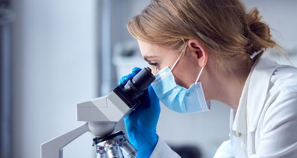 Junge Frau blickt durch ein Mikroskop auf einen Objektträger.