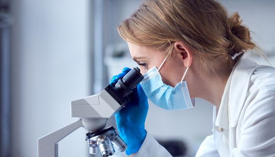 Junge Frau blickt durch ein Mikroskop auf einen Objektträger.