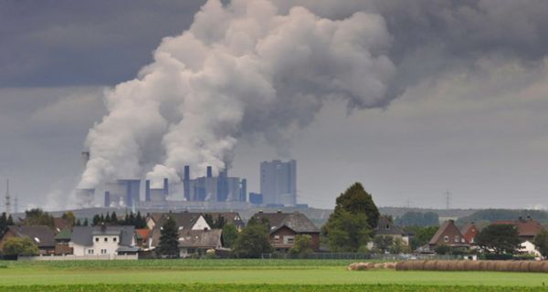 Großes rauchendes Kraftwerk. Davor ein kleines idyllisches Dorf.