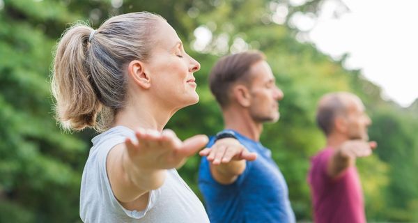 Gruppe von mehreren Menschen, machen draußen Yoga.
