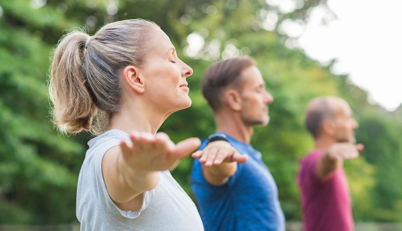 Gruppe von mehreren Menschen, machen draußen Yoga.