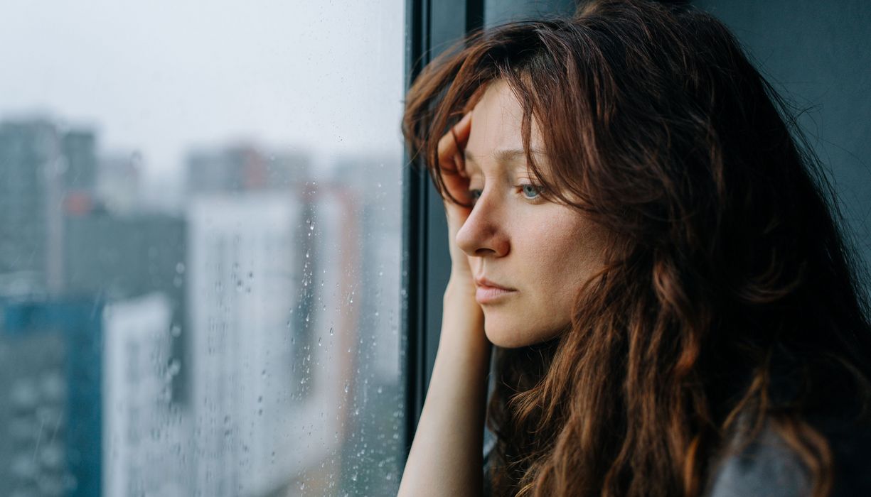 Frau schaut aus einem Fenster, auf dem Wassertropfen sind