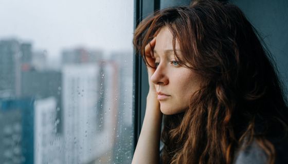 Frau schaut aus einem Fenster, auf dem Wassertropfen sind