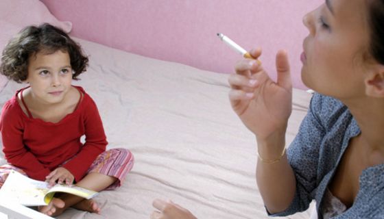 Rauchende Mutter steht am Bett ihres Kindes