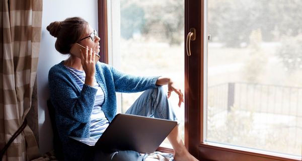 Frau schaut mit Handy am Ohr aus dem Fenster.