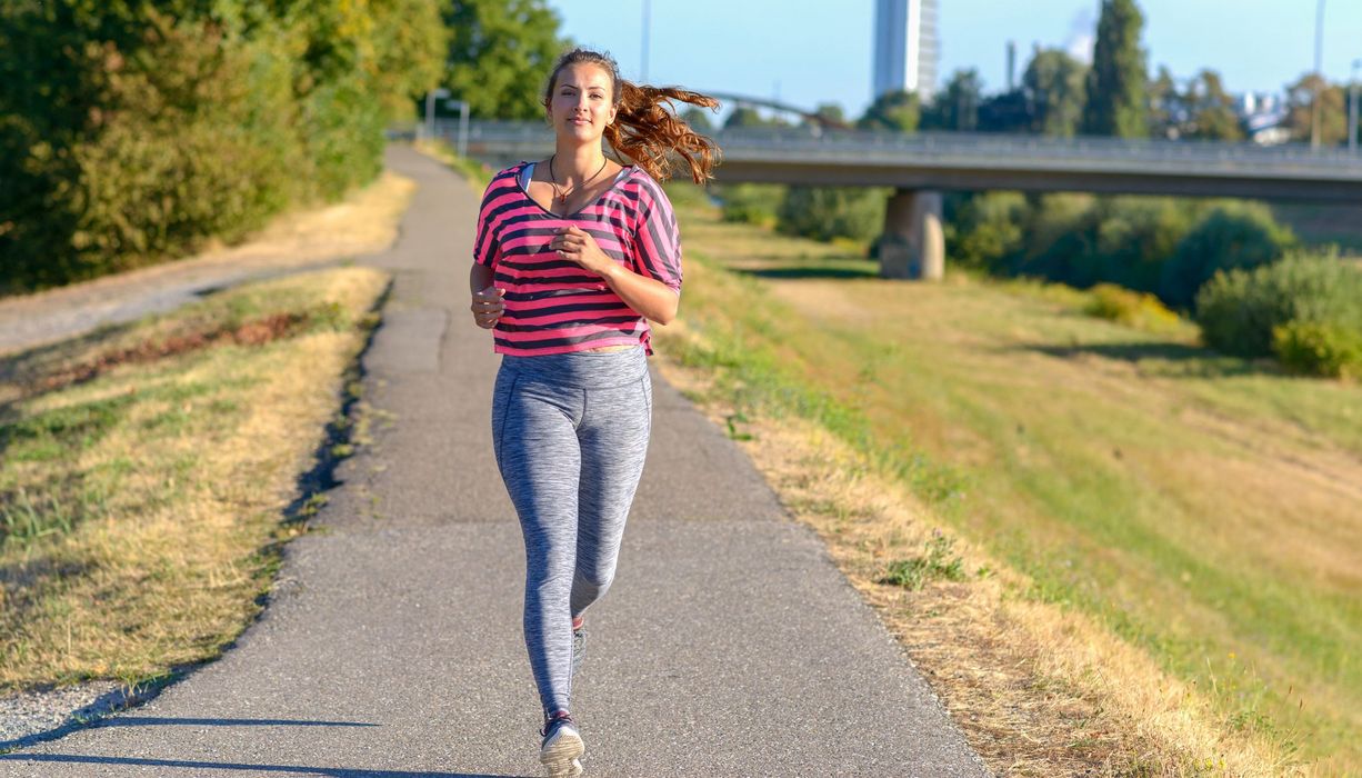 Junge Frau mit leichtem Übergewicht, joggt entlang eines Flusses.