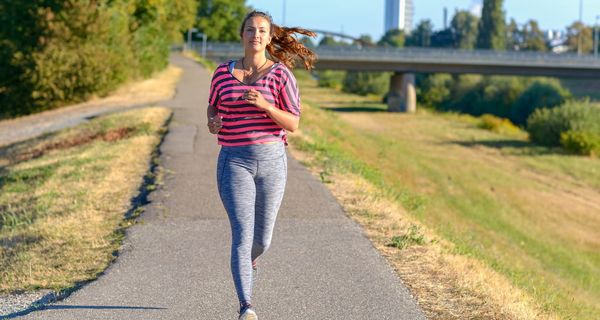 Junge Frau mit leichtem Übergewicht, joggt entlang eines Flusses.