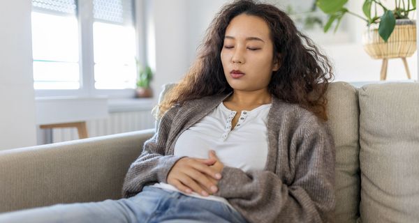 Junge Frau, liegt mit Bauchschmerzen auf der Couch.