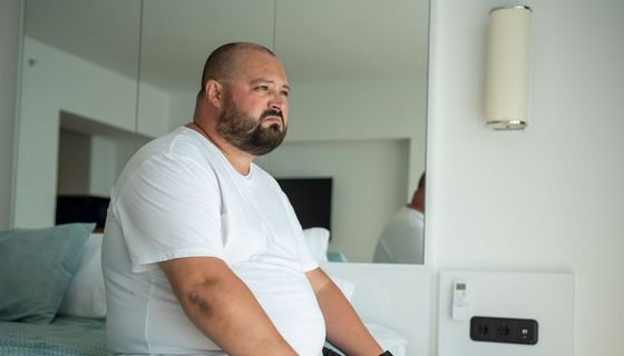 Beleibter Mann sitzt auf einem Bett.