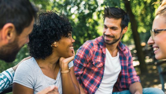 Frau mit Hörgerät unterhält sich fröhlich mit Freunden im Park.