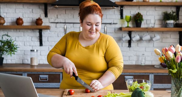 Eine junge, übergewichtige Frau steht in der Küche und schneidet Tomaten.