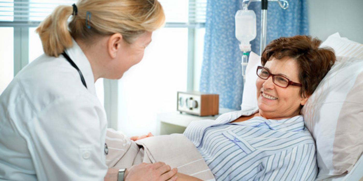 Lächelnde ältere Frau im Krankenhausbett, sie bekommt von einer Ärztin die Hand gehalten