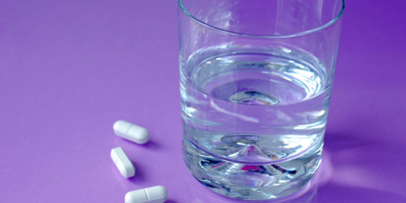 Weiße Tabletten neben Wasserglas