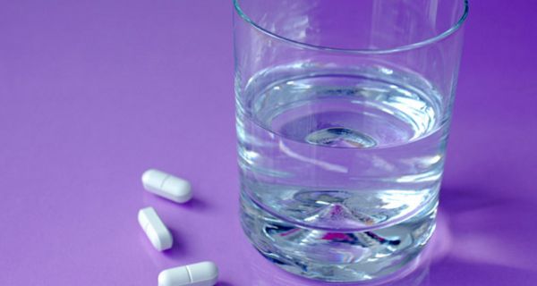 Weiße Tabletten neben Wasserglas