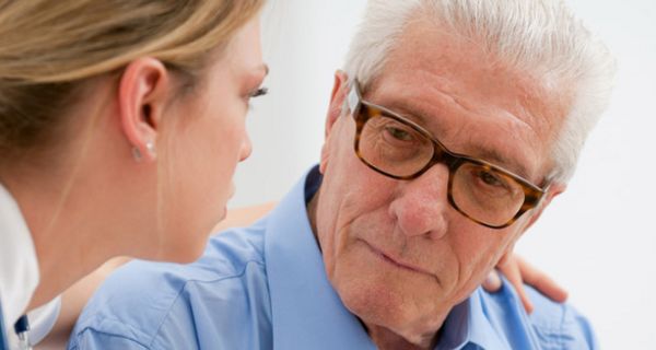 Älterer, deprimiert wirkender Mann bekommt von Krankenschwester Trost zugesprochen