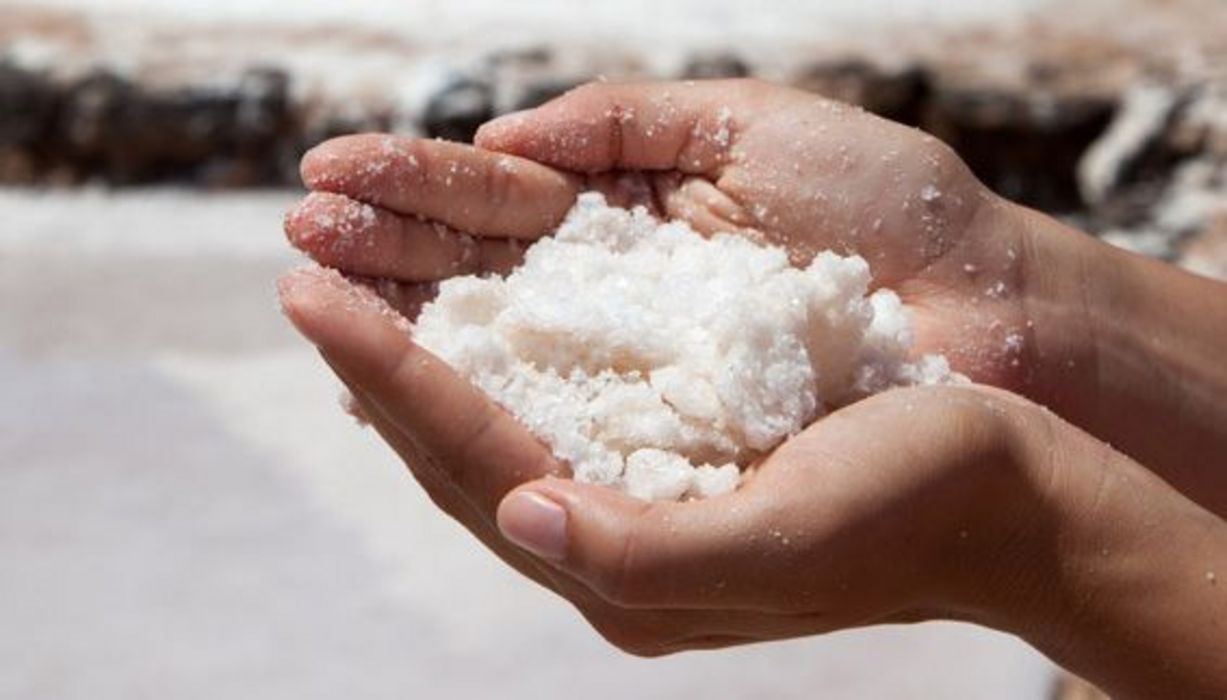 Salzberge im Hintergrund, im Vordergrund groß eine Hand voller Salz