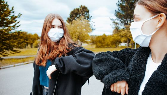 Zwei junge Mädchen mit Maske begrüßen sich mit der Ellenbogen-Begrüßung.