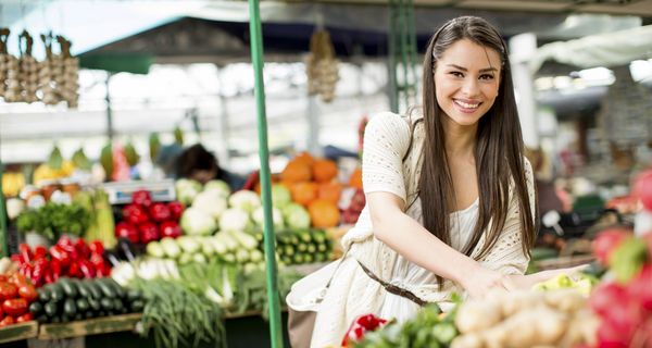 Junge Frau betrachtet einen Marktstand mit Obst und Gemüse.