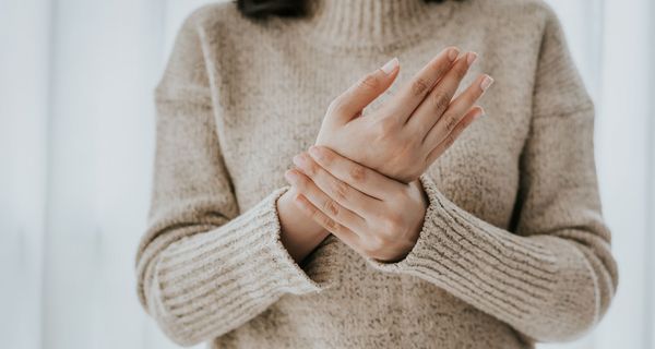 Frau mit Wollpullover, hält mit einer Hand ihre andere Hand fest.